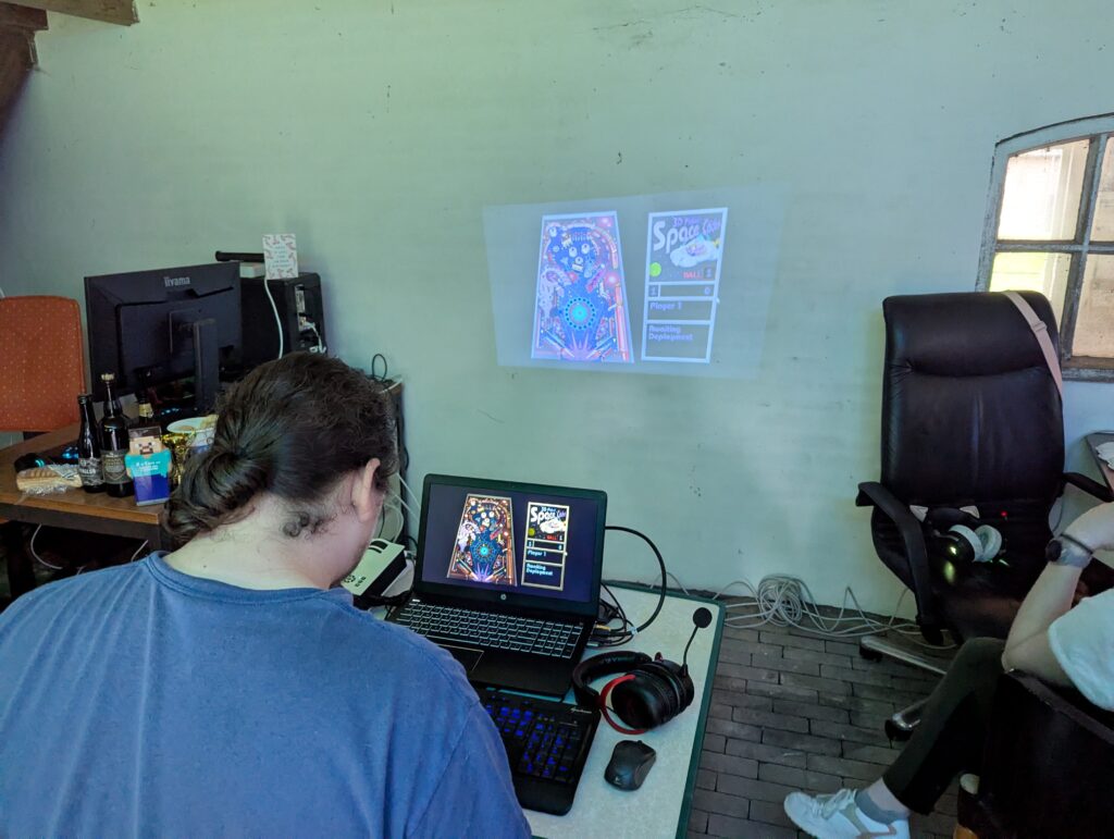 Deelnemer speelt 3D Pinball op een laptop tijdens Loef-LAN LAN-party, met projectie op de muur en andere aanwezigen in de ruimte.